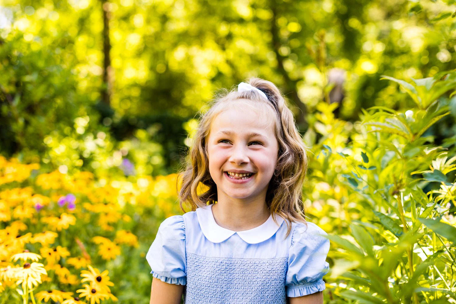 Girl in blue dress smiling in a garden for family portraits